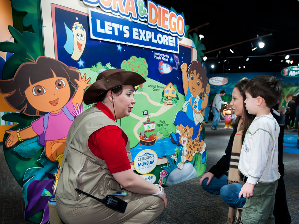 Museum staff member talking with family at entrance to Dora and Diego: Let's Explore exhibit.